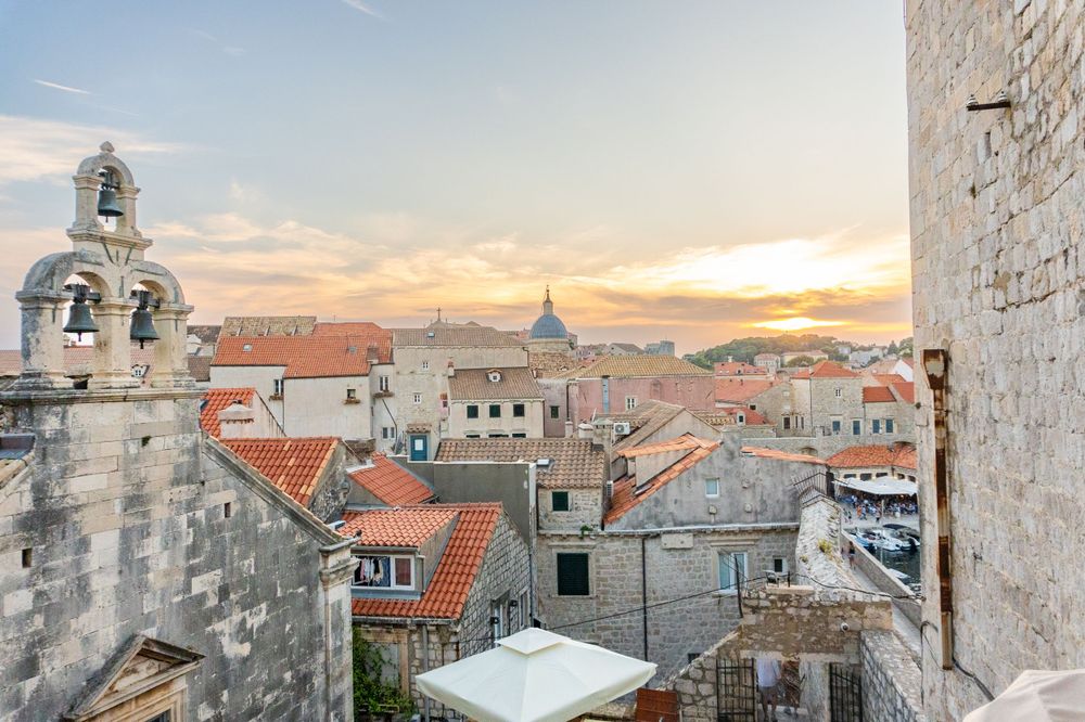 Historic rooftops and bell tower of Dubrovnik's Old Town at sunset with orange sky in Croatia.
