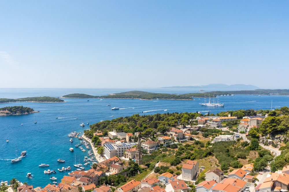 Aerial view of Hvar harbor with boats anchored in turquoise waters surrounded by Mediterranean architecture.