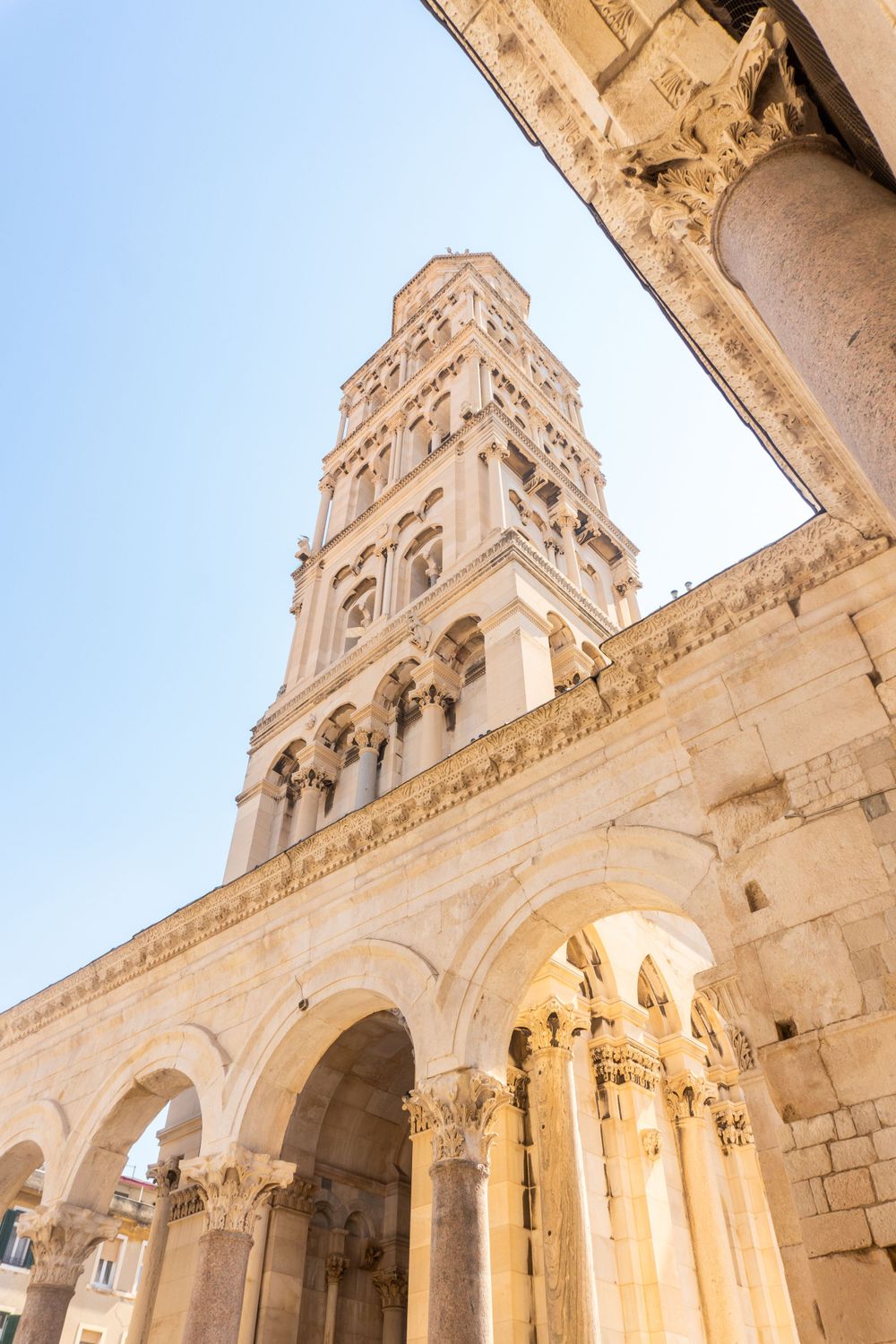 Cathedral bell tower with ornate stone architecture and arches against bright blue sky in Split, Croatia.