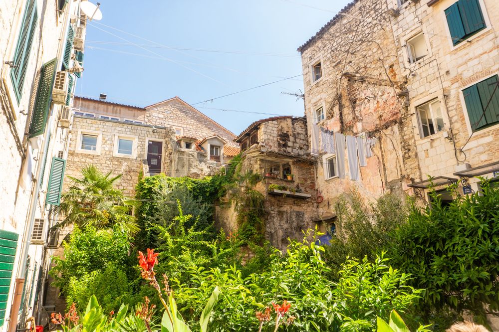 Overgrown courtyard with lush plants and flowers between old stone buildings in Mediterranean town.