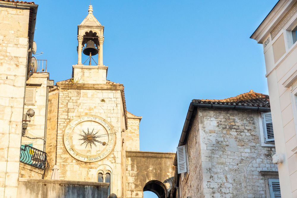 Historic clock tower and stone buildings in Split's old town against bright blue sky.
