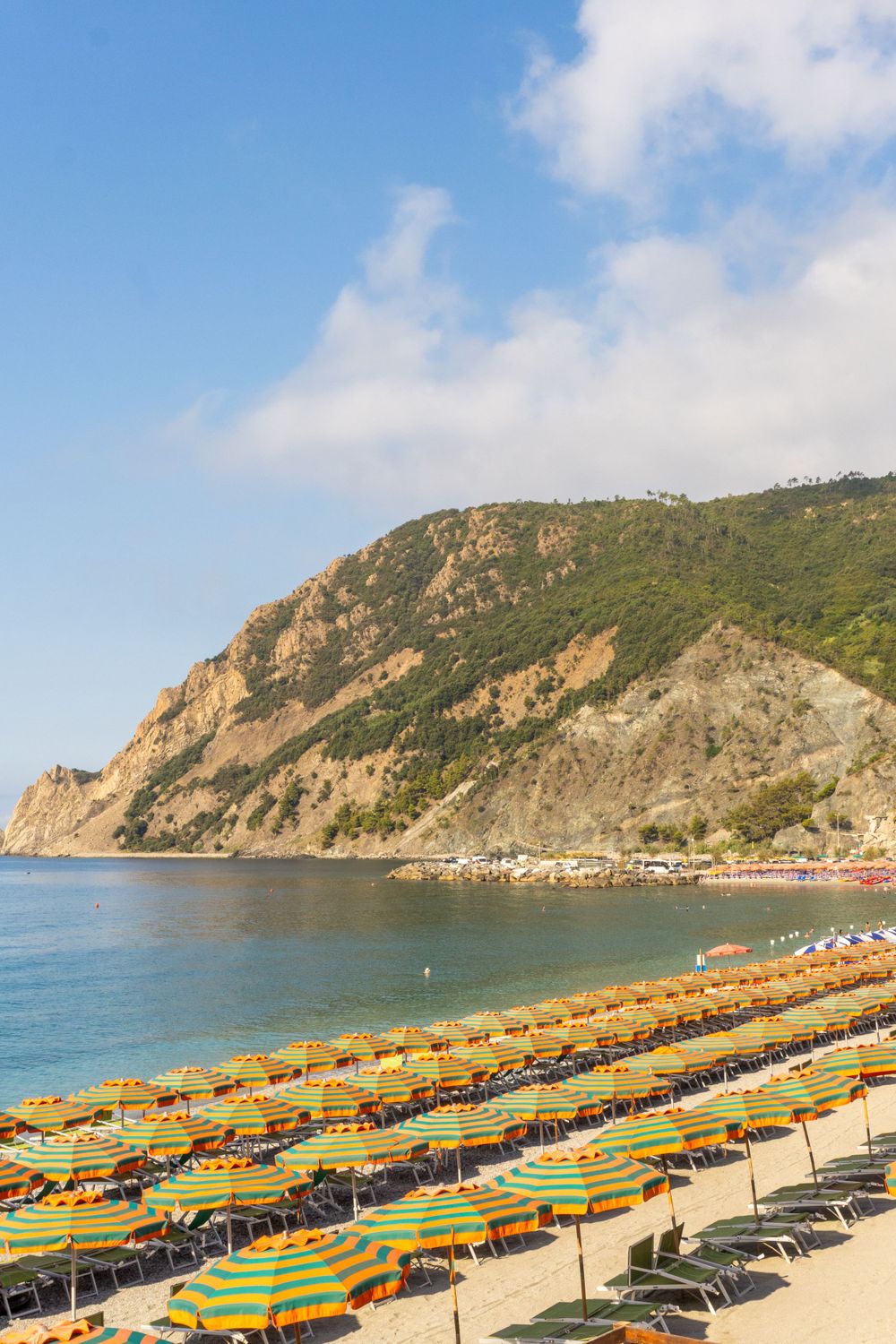 Colorful beach umbrellas line a Mediterranean beach with dramatic cliffs rising from turquoise waters.