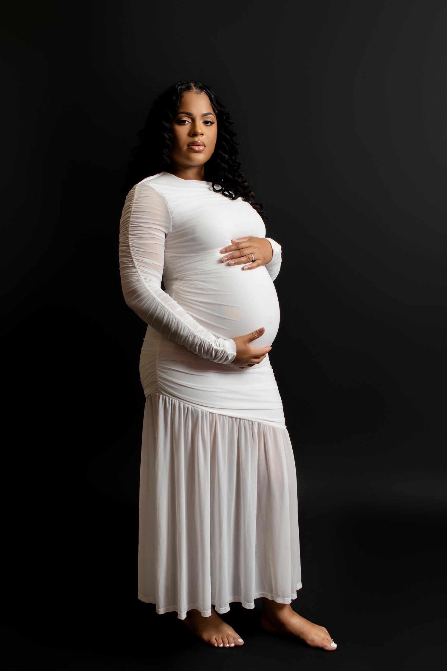 Studio maternity photos against black background showing woman in flowing white dress.