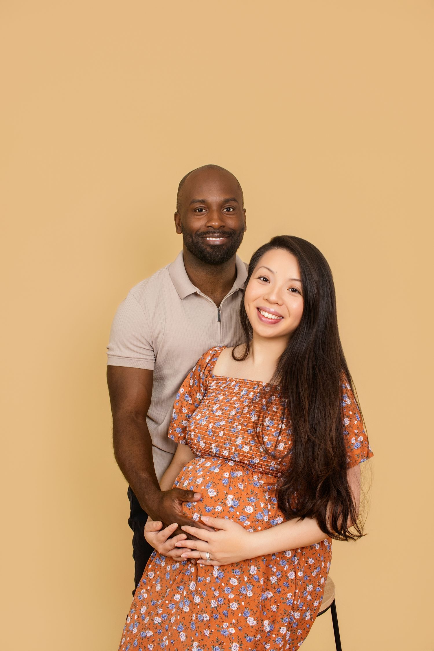 Intimate maternity portrait with couple embracing against warm beige background.
