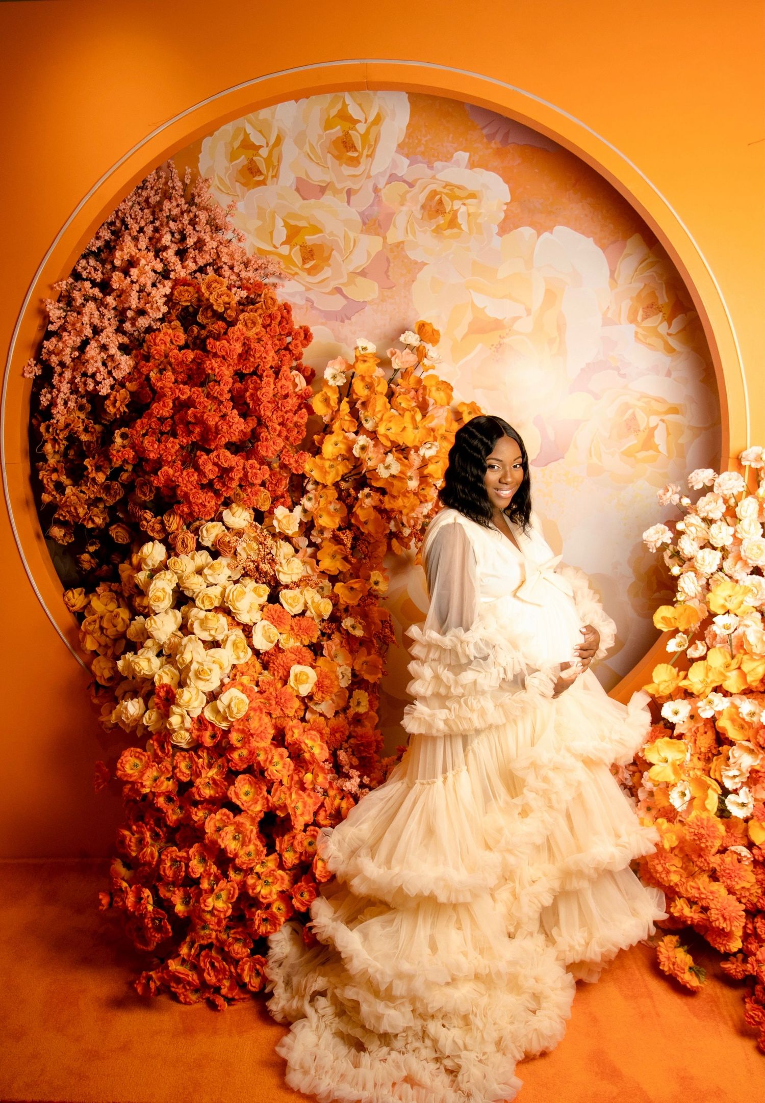 Ethereal portrait in flowing white gown against floral arch with orange lighting.