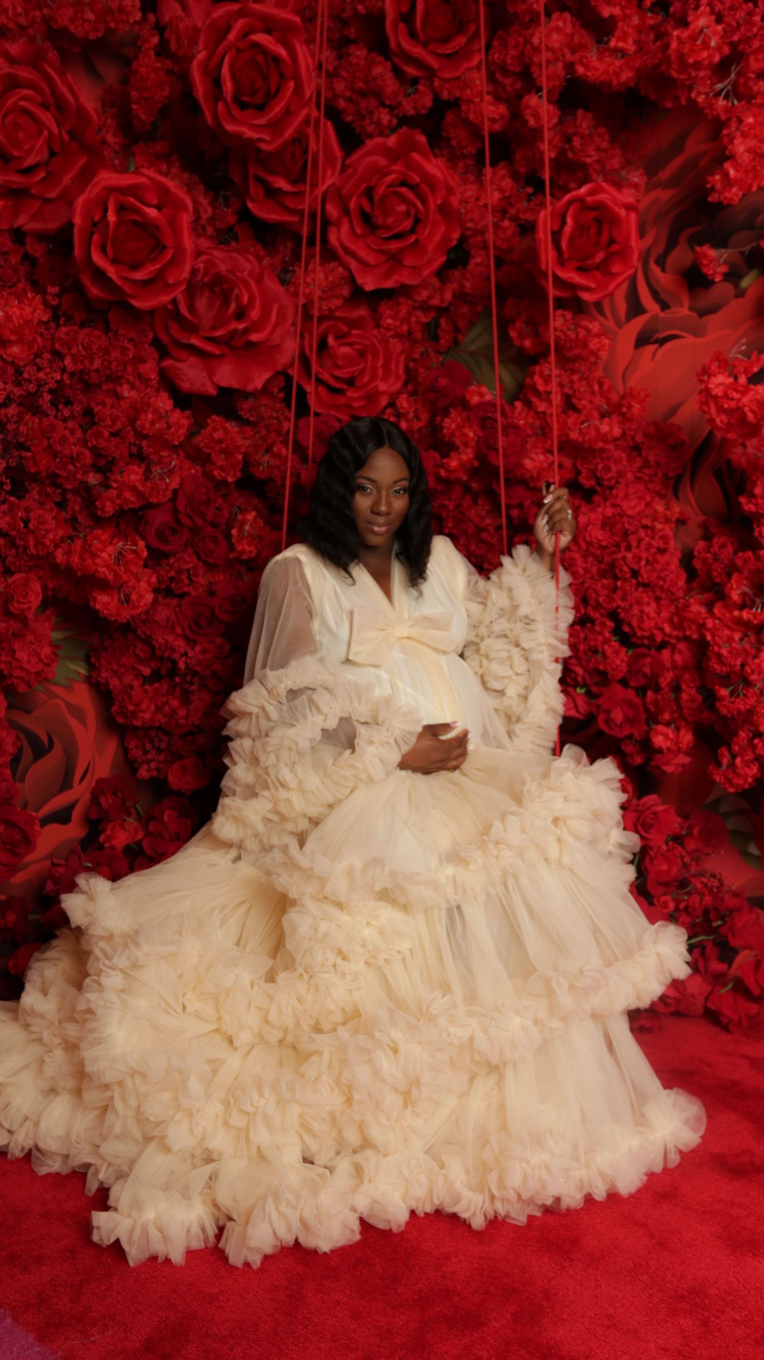 Dramatic portrait with flowing white gown against red rose wall backdrop.