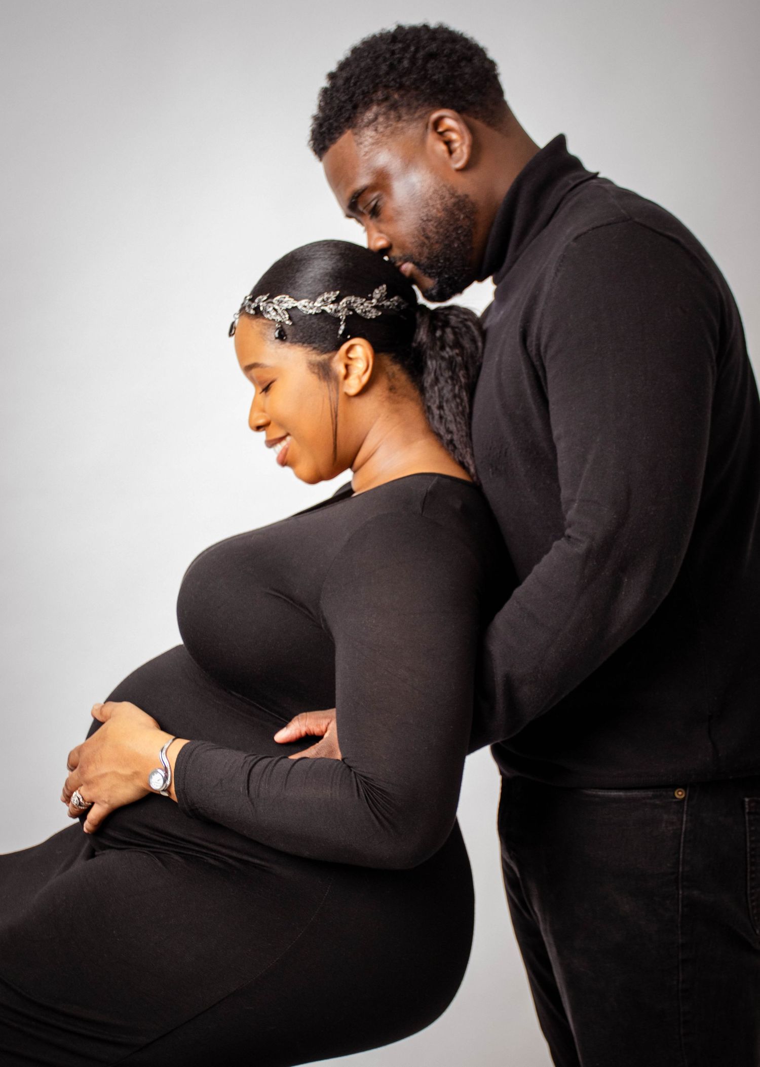 Intimate side view of expecting couple in black clothing during maternity photoshoot.
