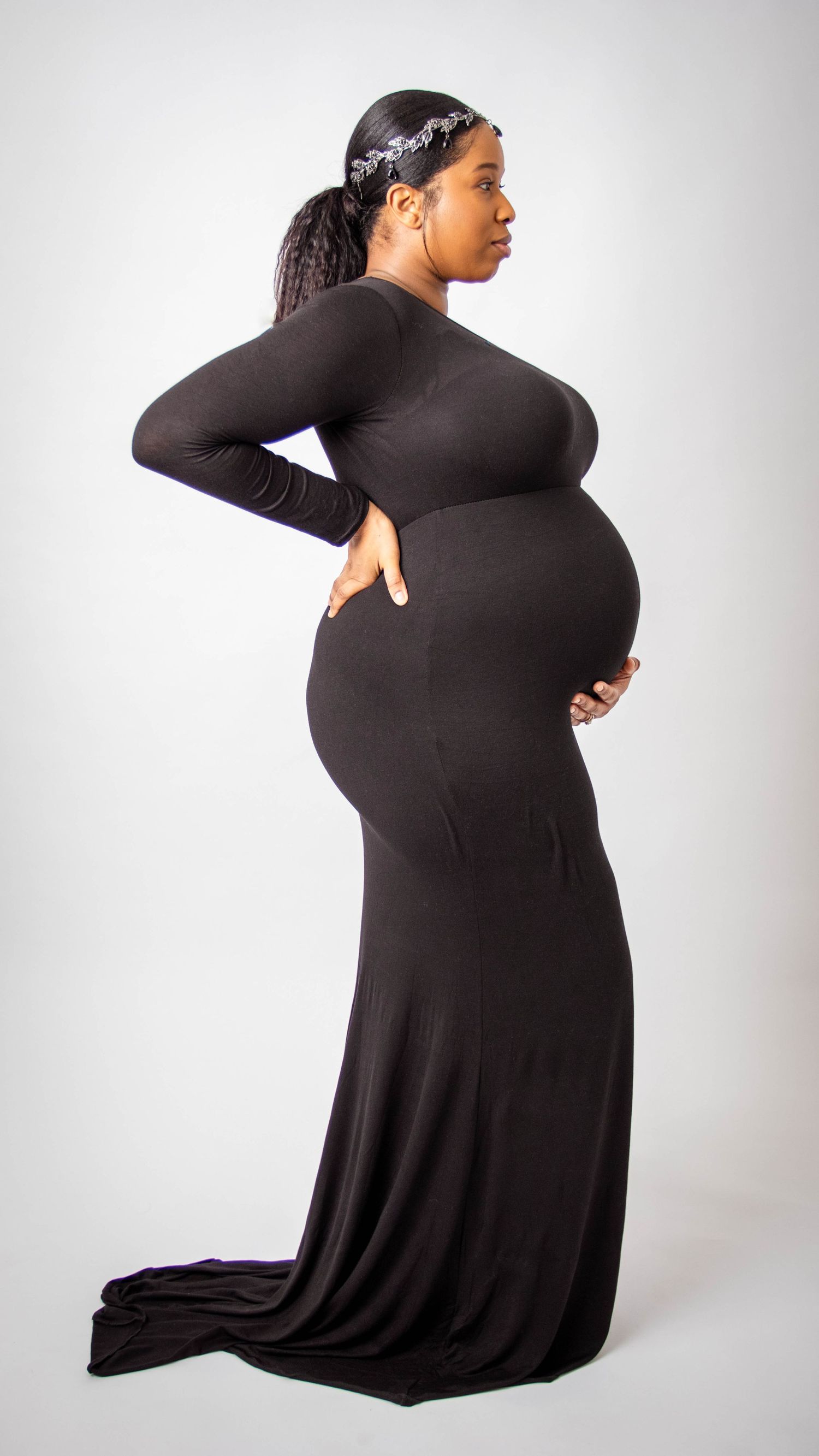 Side profile of pregnant woman in long black dress showing her baby bump.