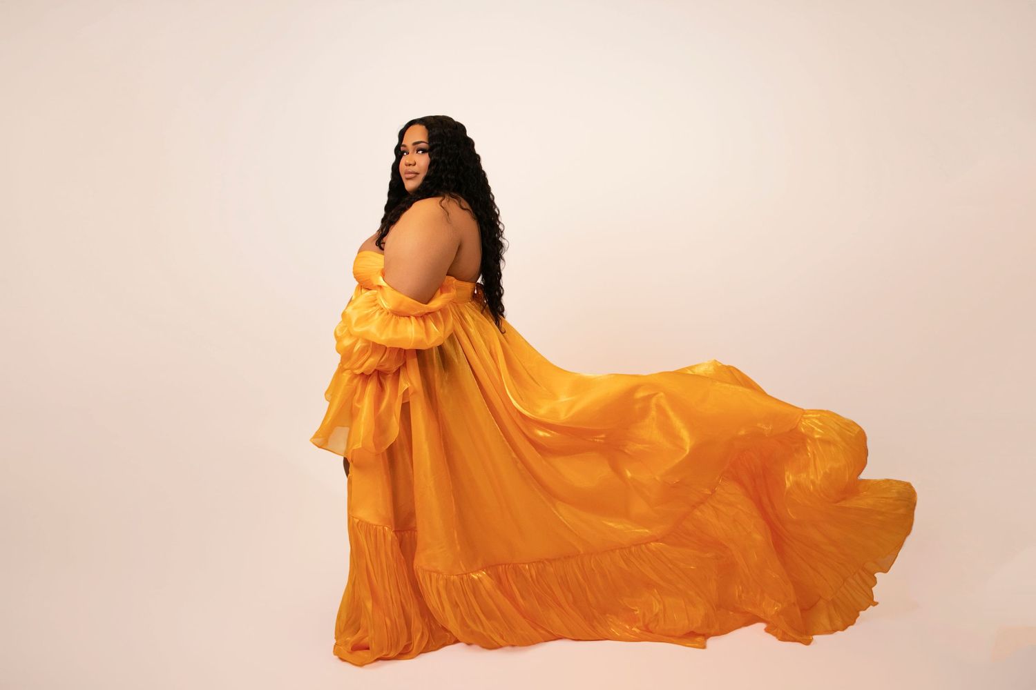 A dramatic fashion series with flowing orange fabric creating movement against neutral backdrop.