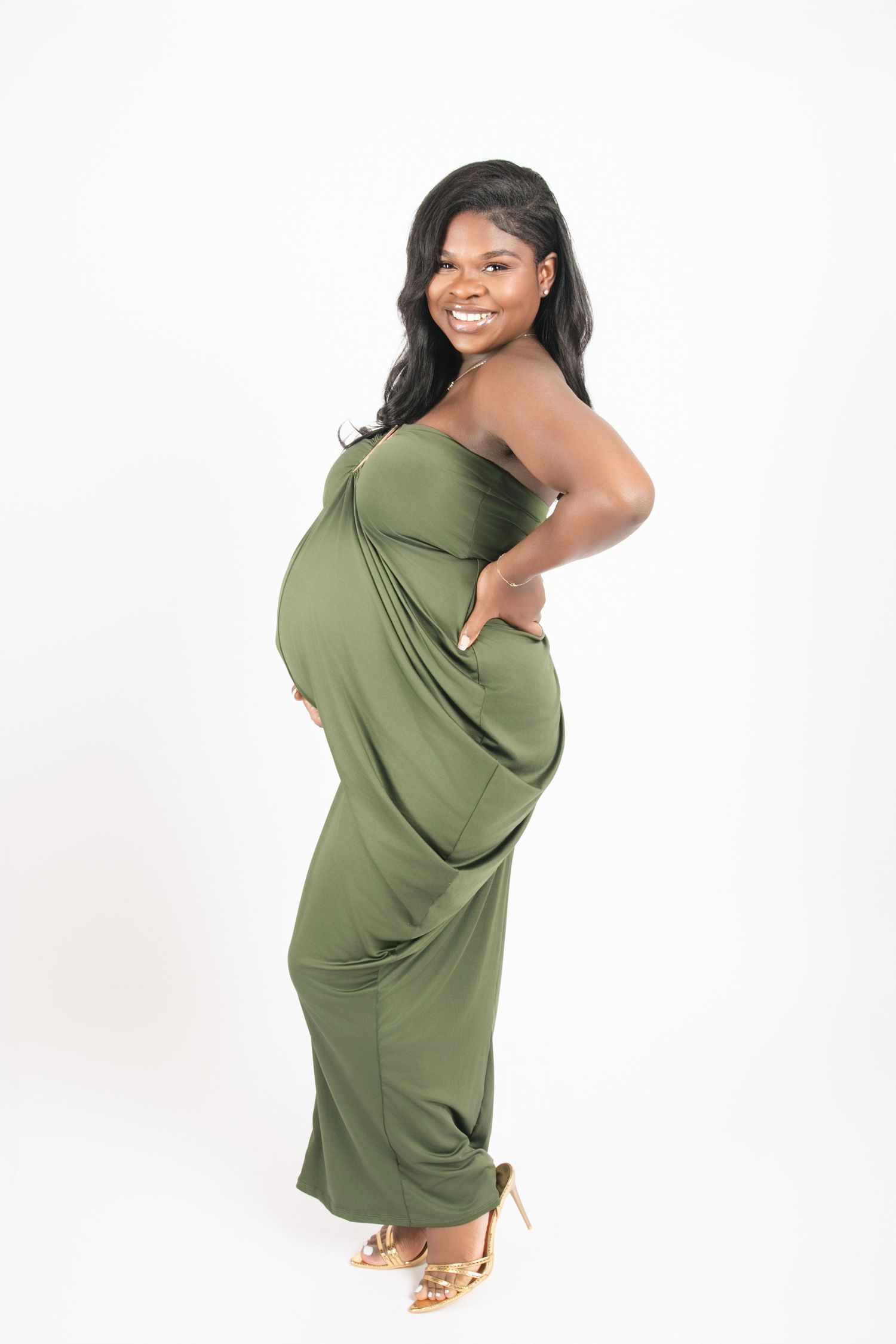 Model wearing olive green dress poses dynamically against white background.