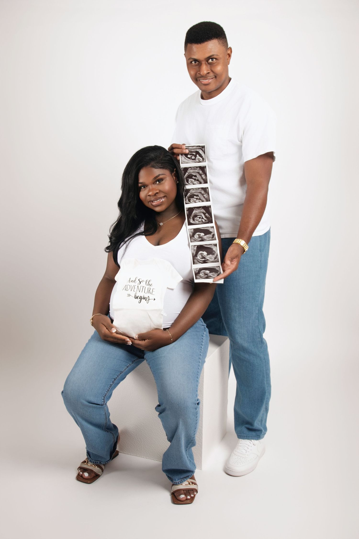 Maternity photoshoot featuring couple in white shirts and jeans showing ultrasound photos.