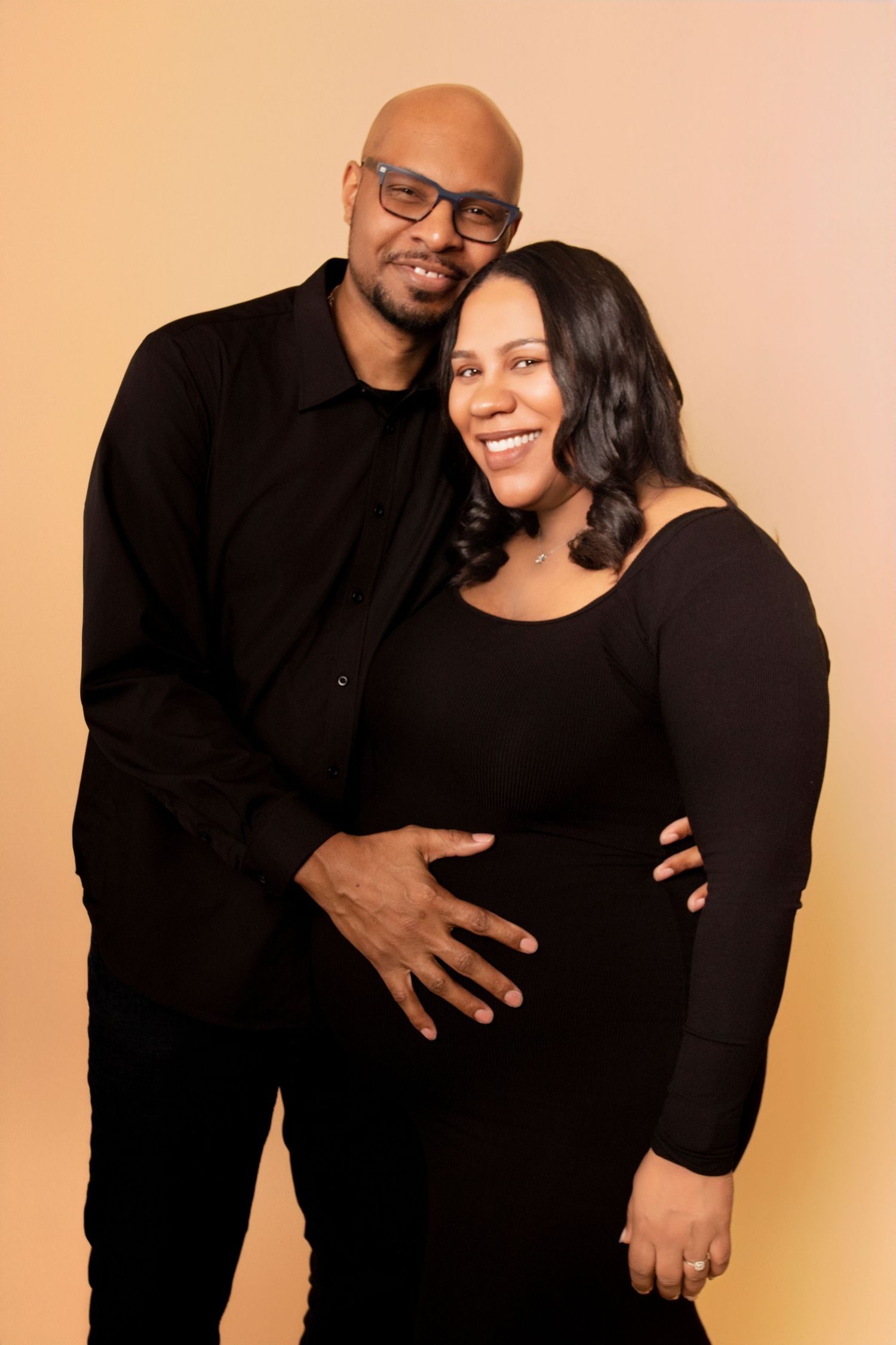 A couple shares loving embraces in black outfits during their maternity studio session.