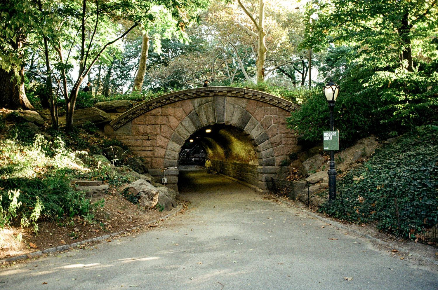 Stone archway tunnel path through green foliage in Central Park.