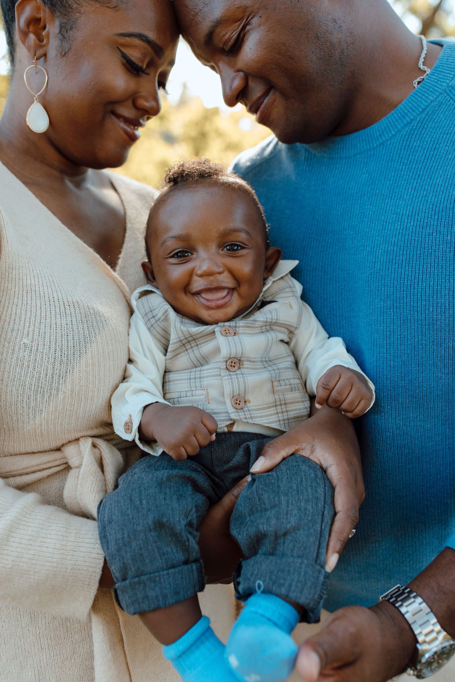 Parents in neutral sweaters sharing a tender moment with their baby wearing blue booties.