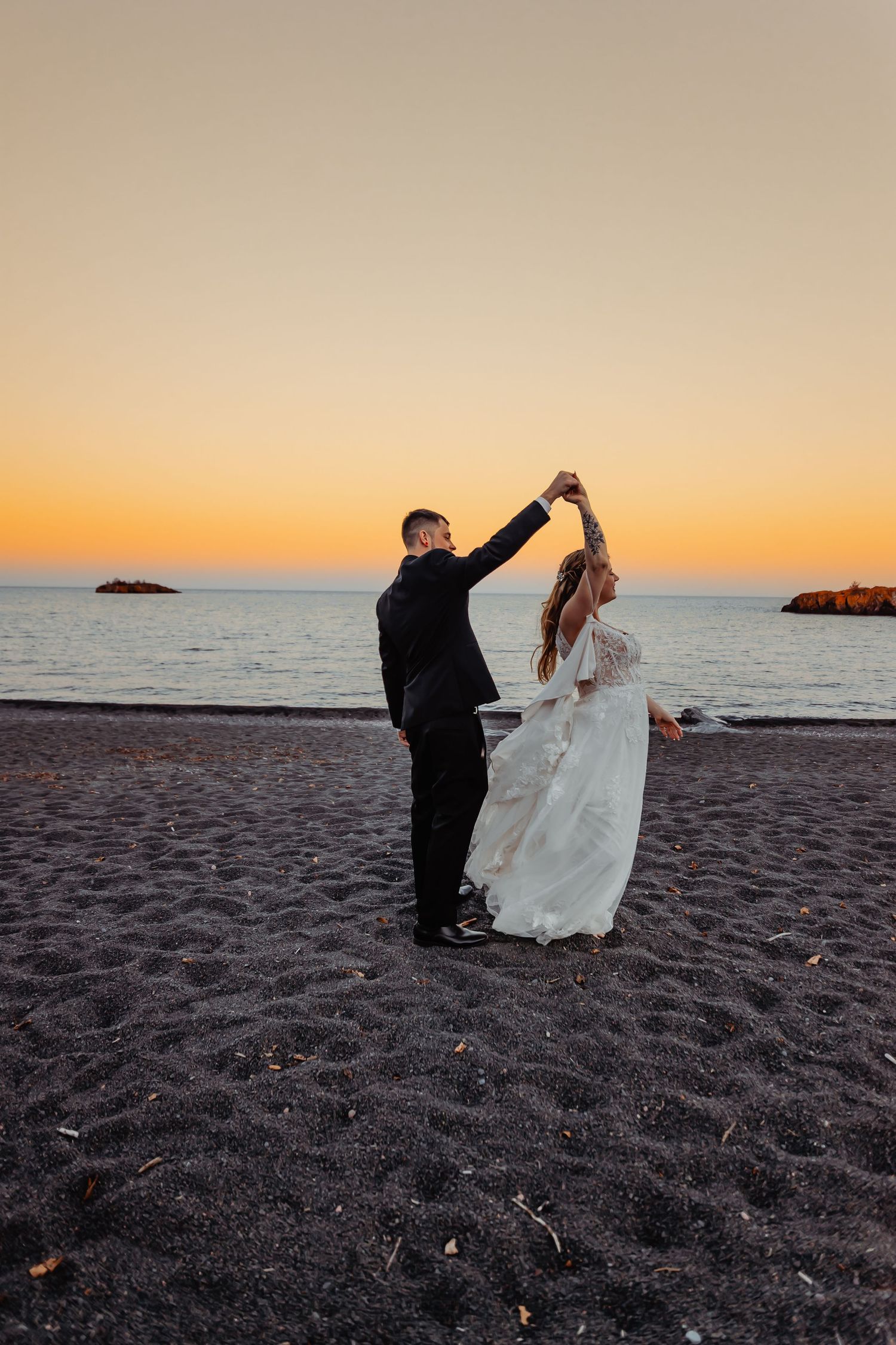A couple dances on a beach at sunset with the ocean in the background.
