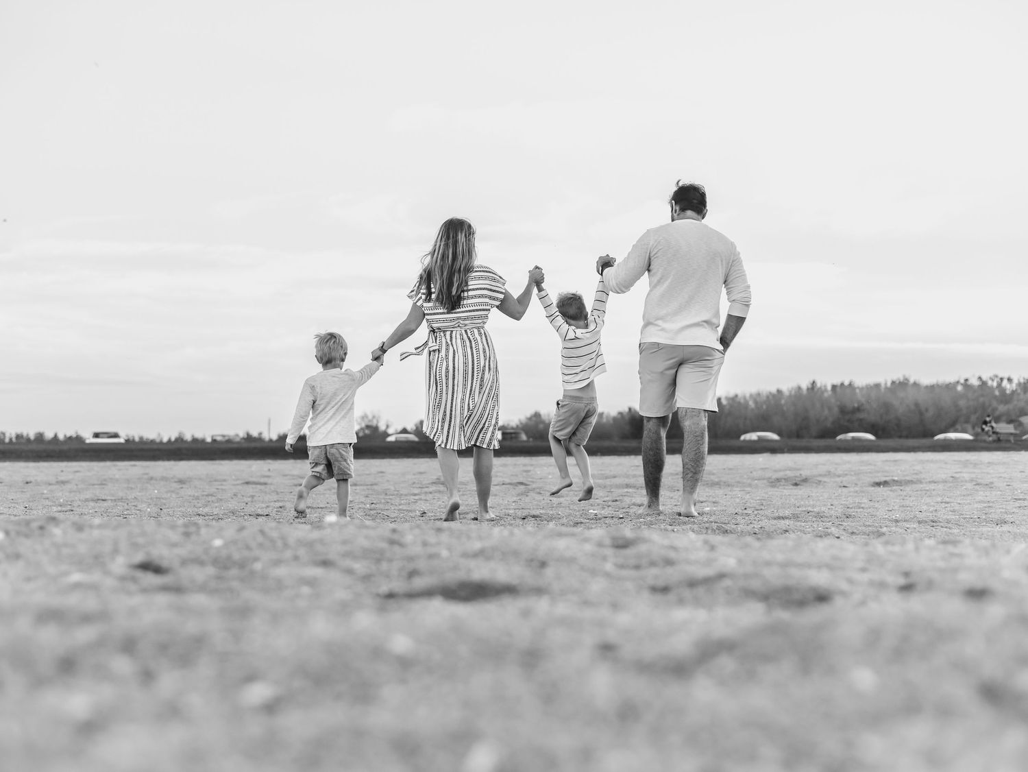 Black and white photo of a family holding hands while running together on a beach.