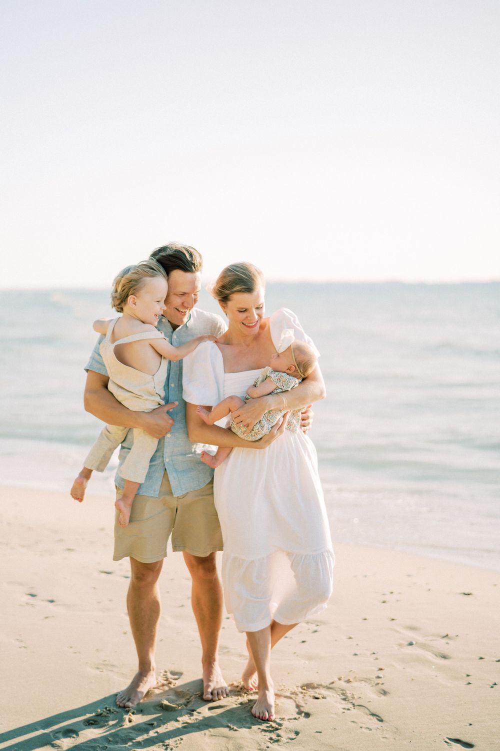 A family walks together along the shoreline during a sunset beach photoshoot.