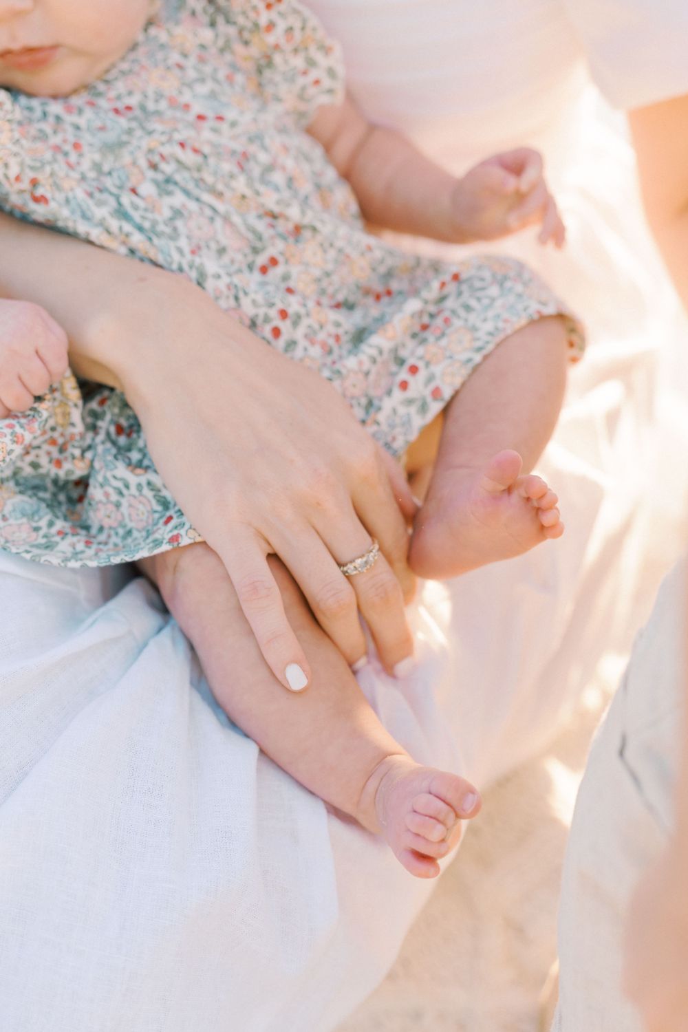 Close-up of tiny baby toes and hands against a floral patterned fabric in soft natural lighting.