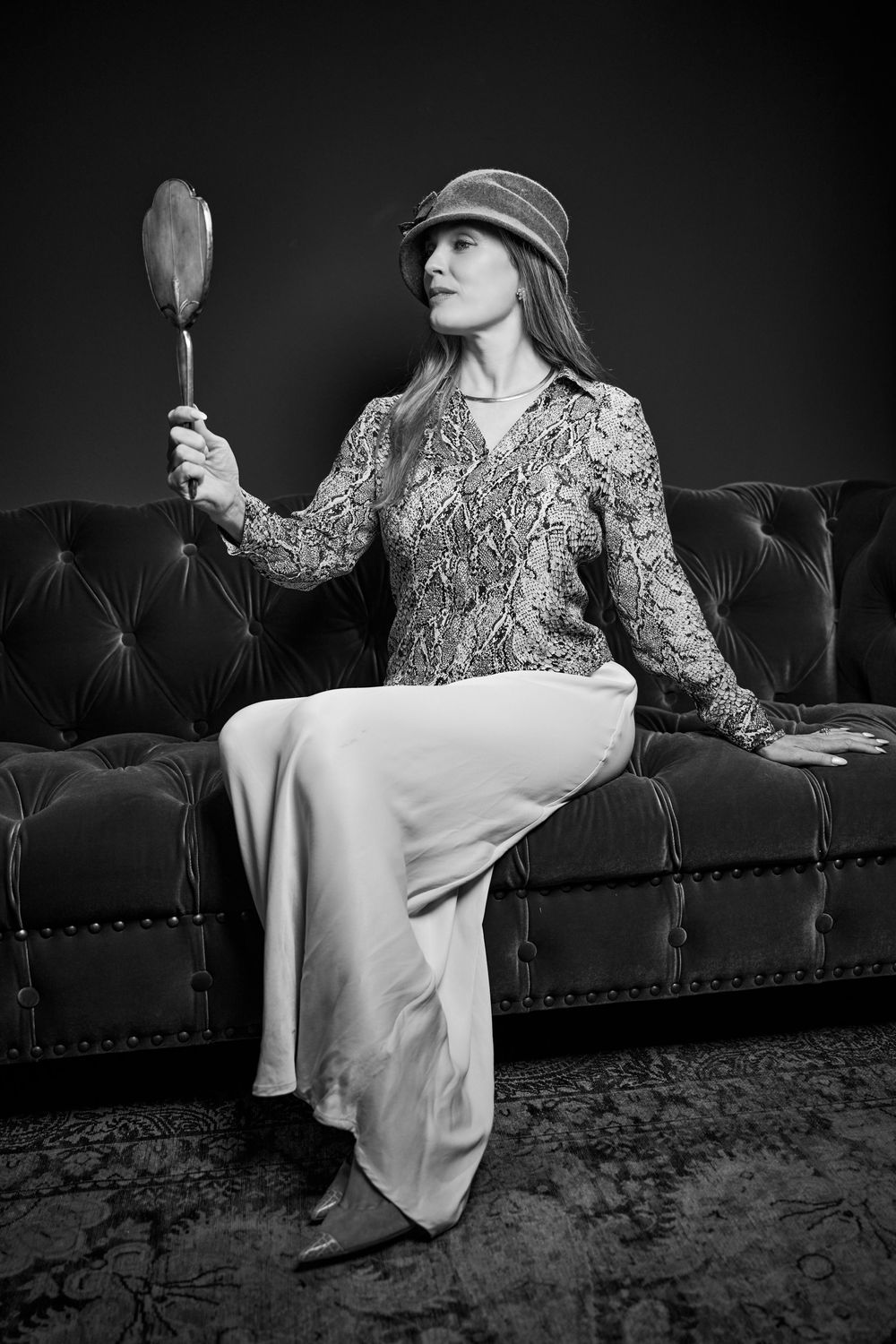 A person in floral patterned clothing reclines elegantly on a tufted velvet couch in dramatic black and white lighting.