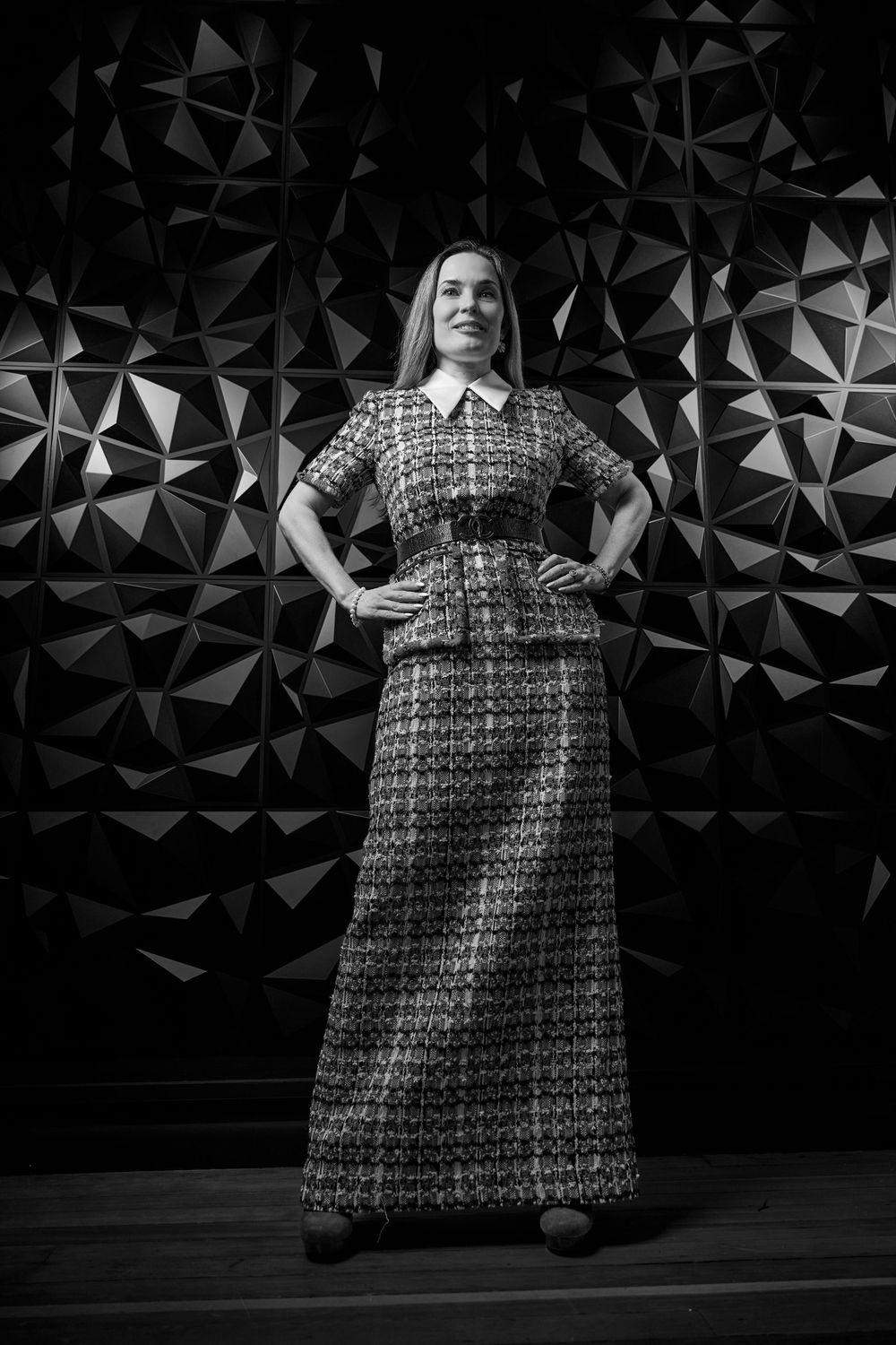 A black and white portrait shot against a geometric background showing a person in a long patterned maxi dress.
