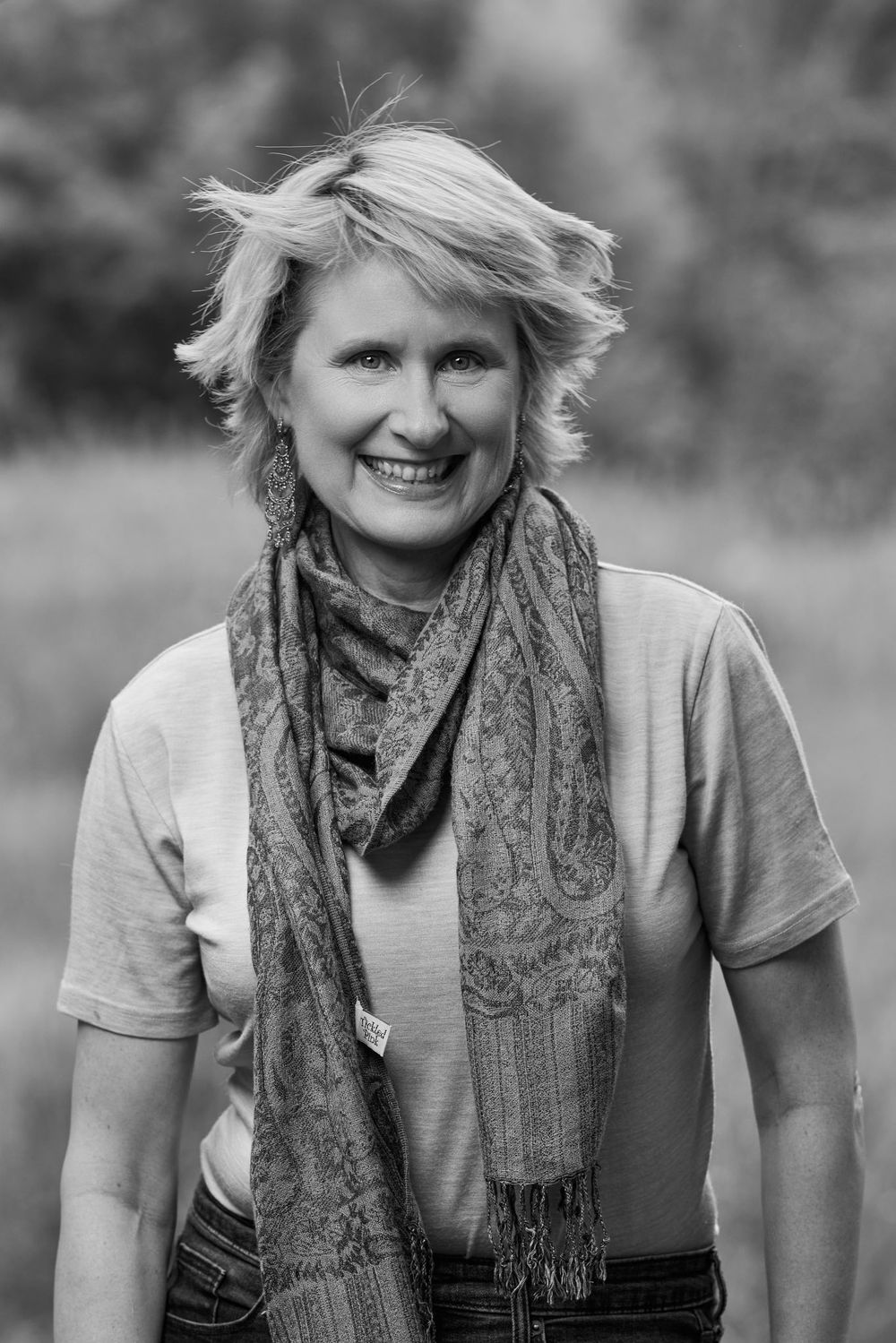 Black and white portrait of someone wearing a patterned scarf and casual t-shirt smiling outdoors.