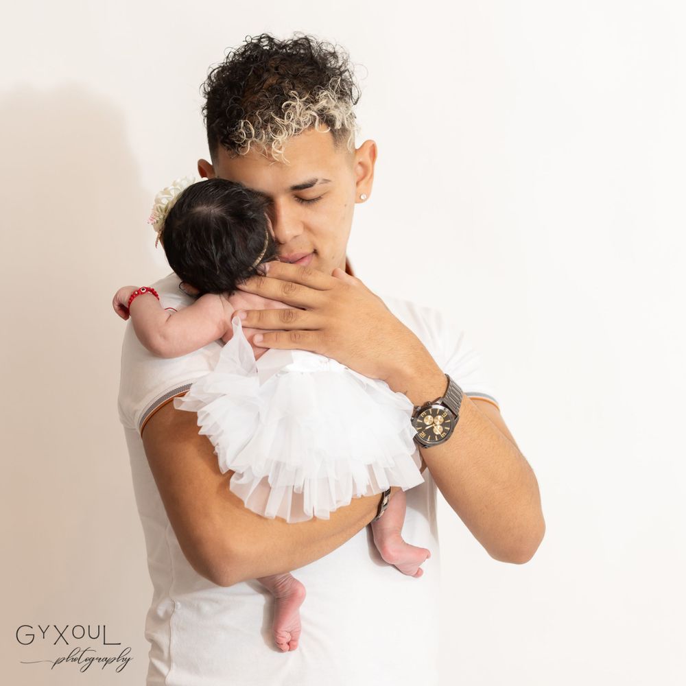 Tender moment with baby wearing white tulle dress being held against white background.
