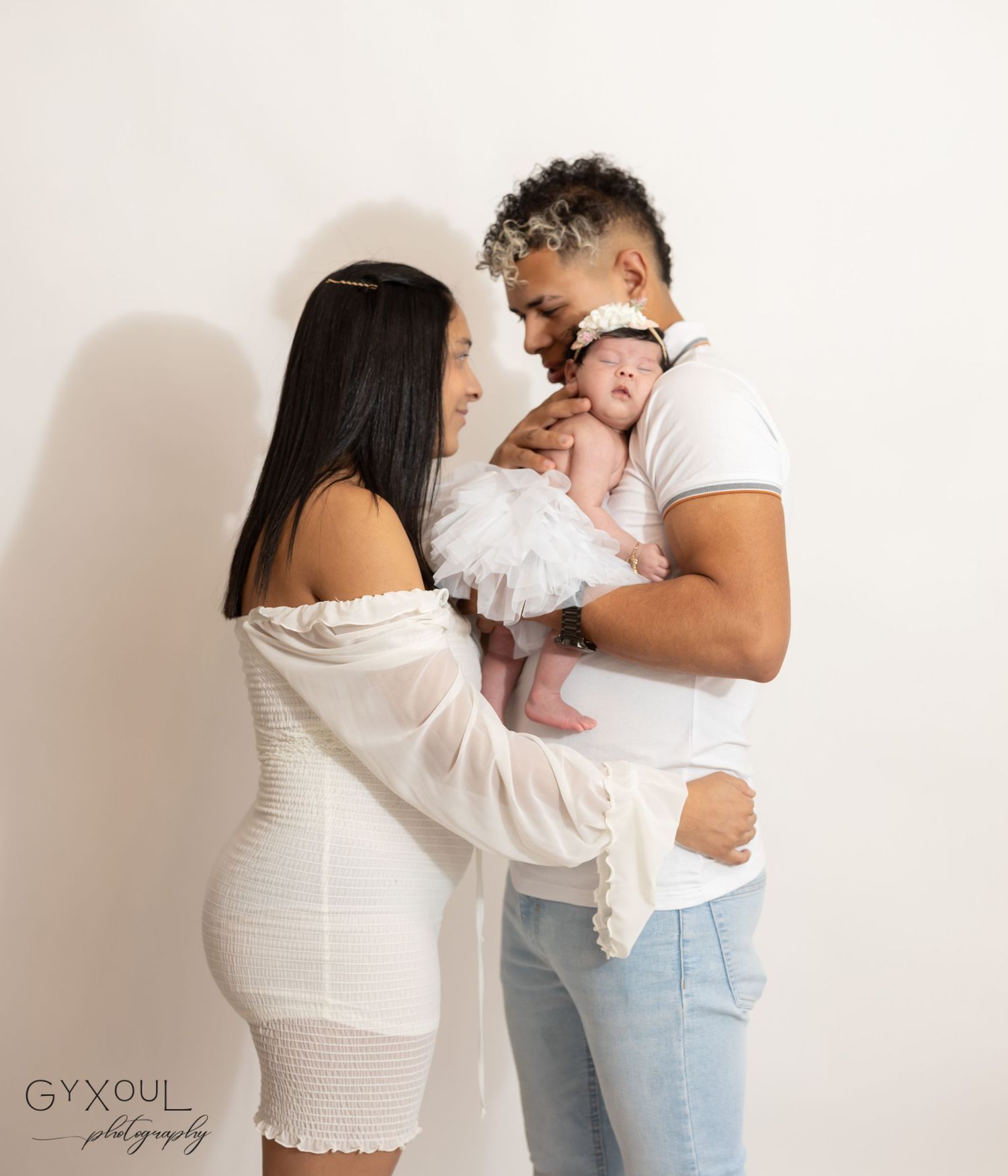Intimate family portrait against white background with baby in white tulle outfit.