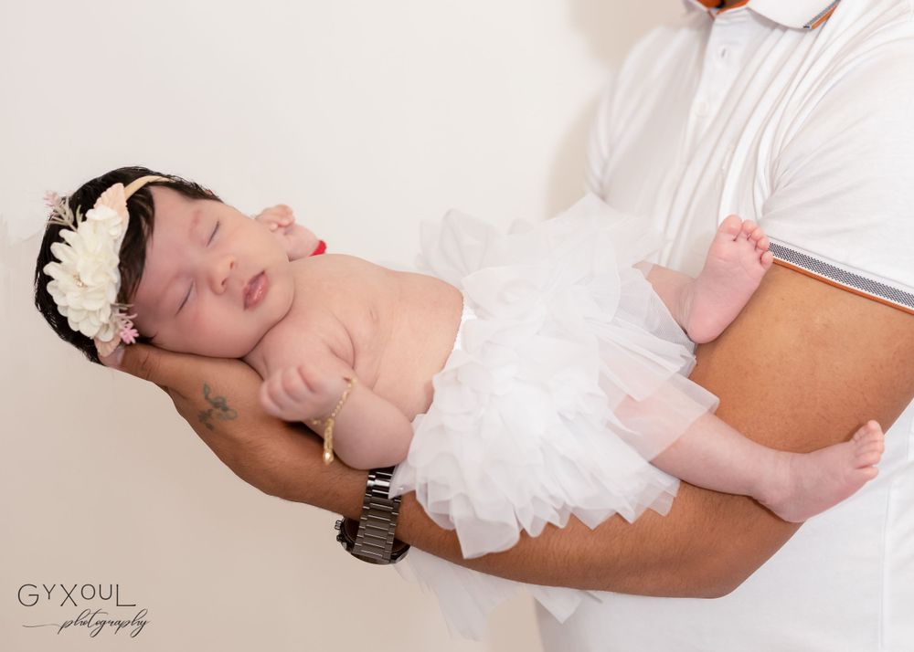 Newborn baby wearing white tulle dress and headband during professional photo session.