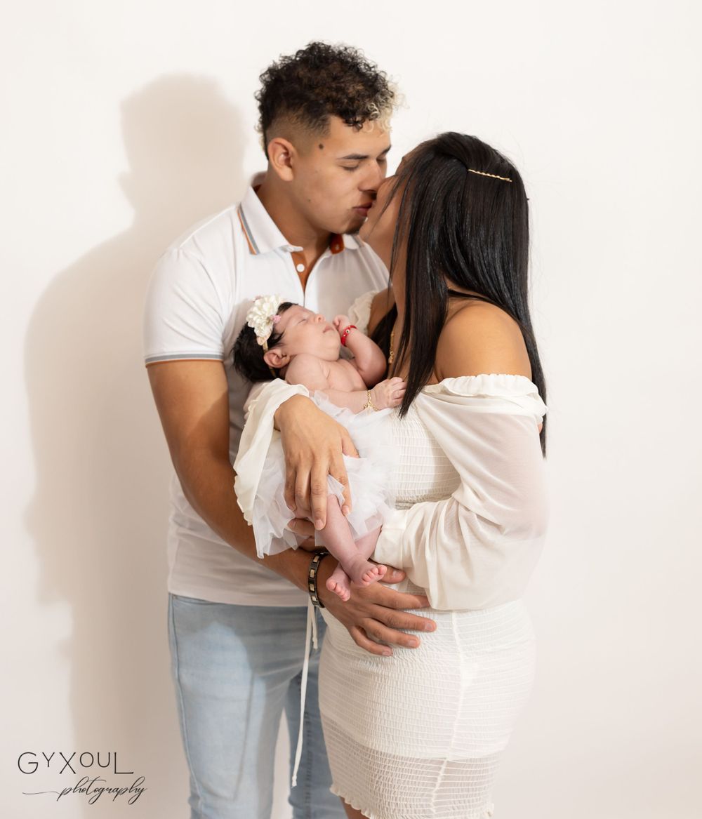 Candid family moment with baby in white dress against studio backdrop.