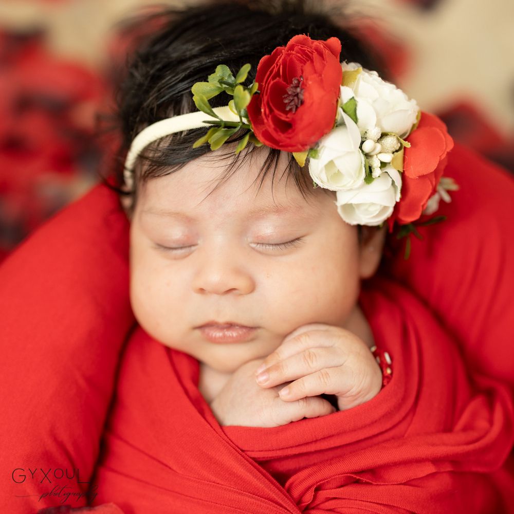 Peaceful sleeping newborn in red wrap with floral headband close-up portrait.