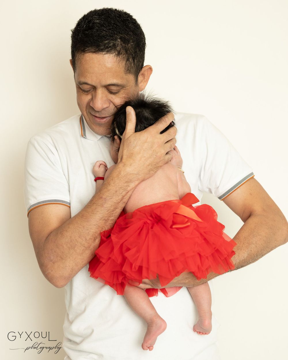 A tender moment of someone in white holding a baby wearing a red tutu dress.