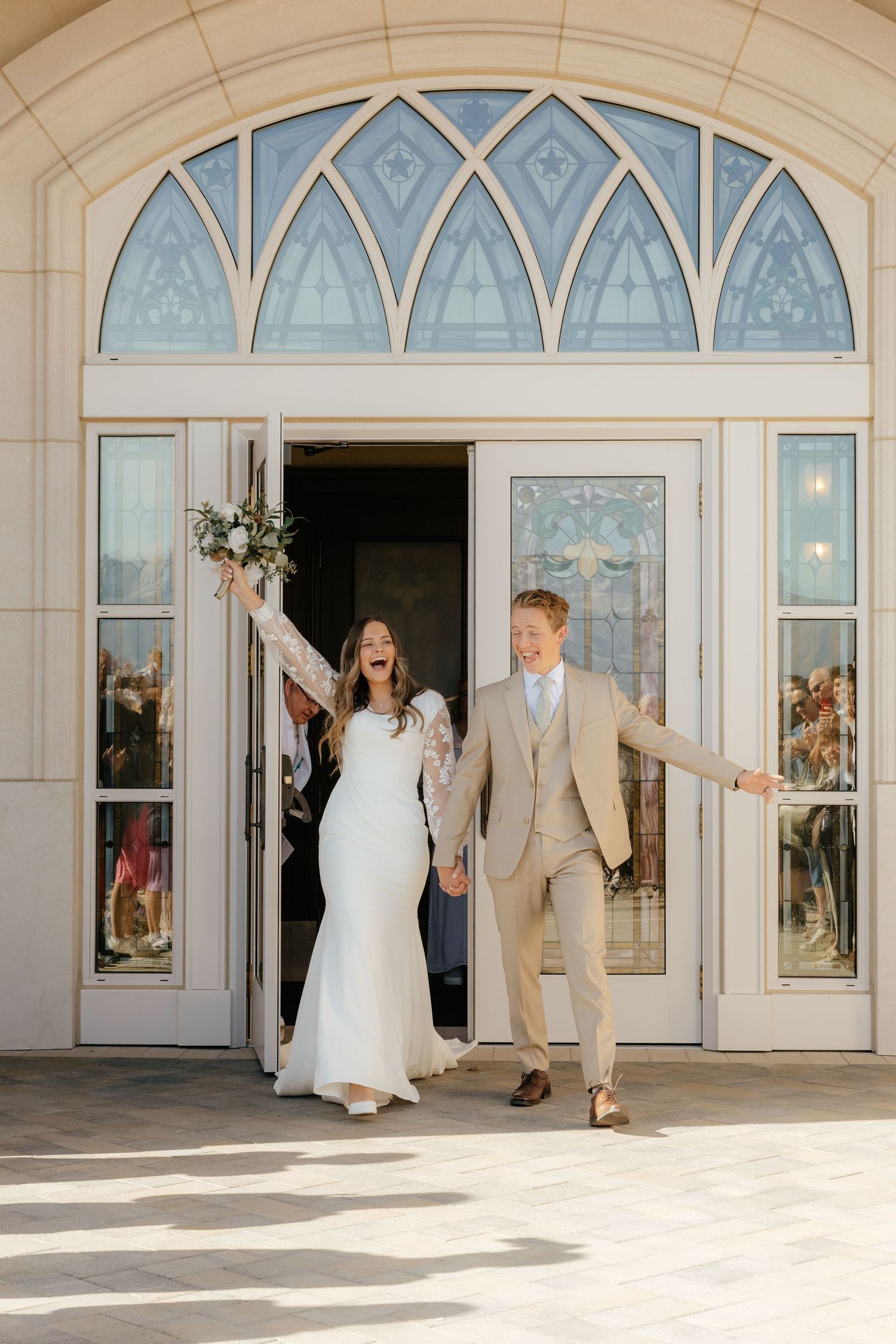 Joyful bride and groom exiting through ornate arched doors of an LDS temple after their wedding ceremony.