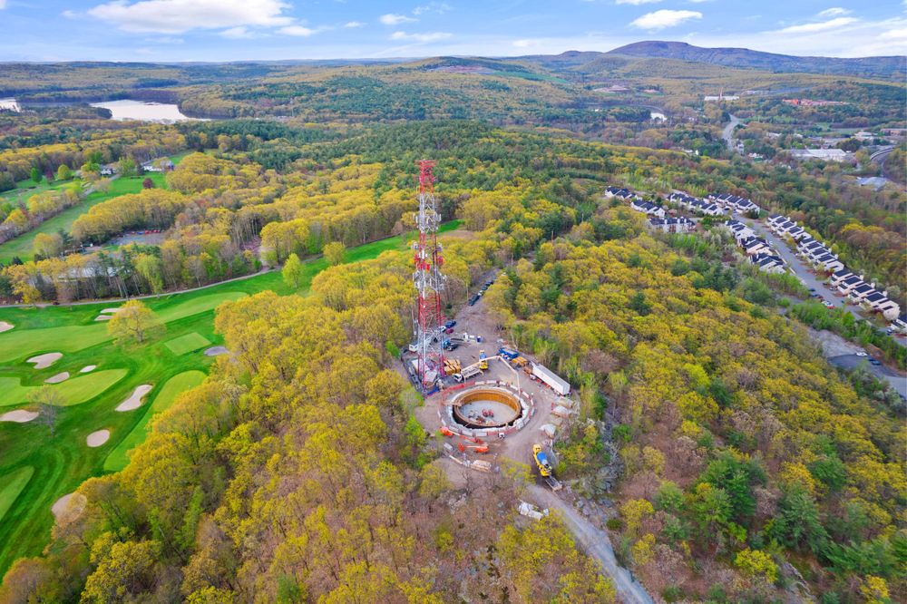 Aerial view of a golf course and circular construction site nestled in autumn foliage with mountains in background.