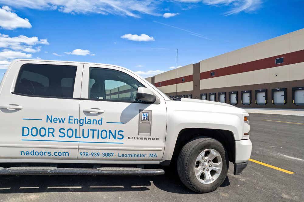 White pickup truck with New England Door Solutions branding parked in front of loading dock.