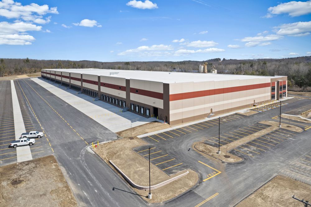 Aerial view of long commercial warehouse building with loading docks and expansive parking area.