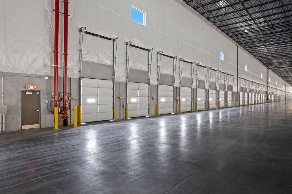 Long row of loading dock doors inside empty industrial warehouse with concrete floor.