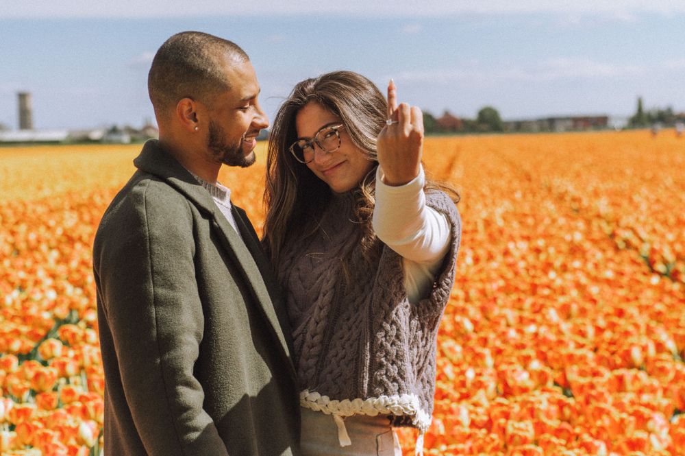 Couple embracing in a vibrant orange tulip field during sunset.