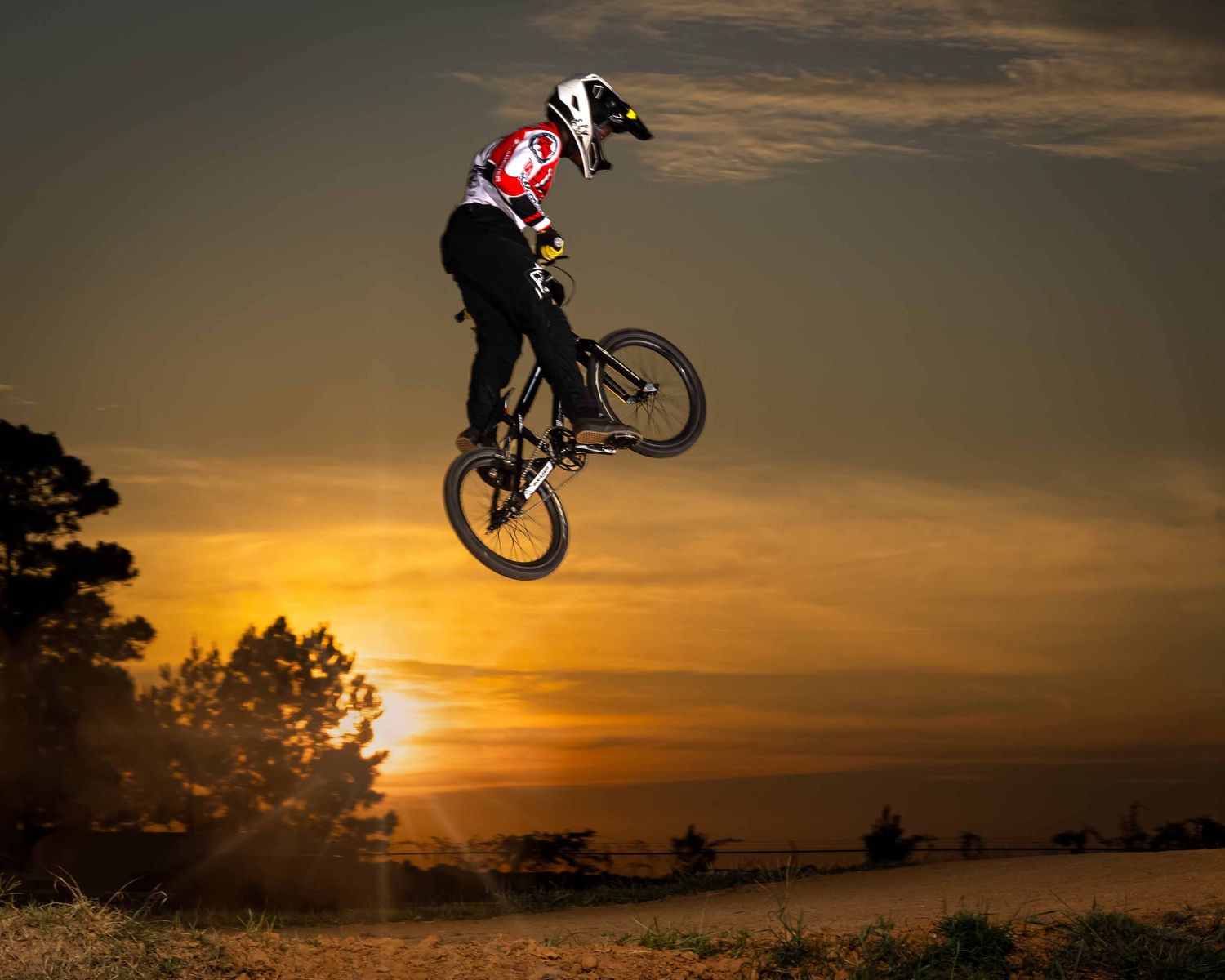 BMX rider performs a dramatic aerial trick silhouetted against a vibrant orange sunset sky.