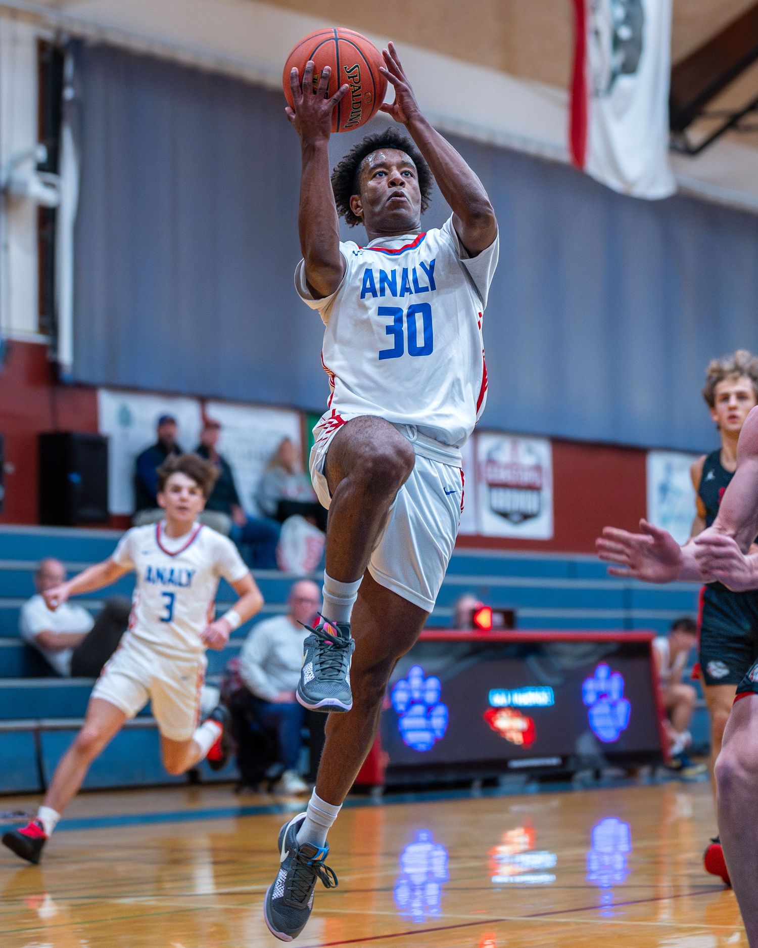 Basketball player leaps for a shot during competitive game in school gymnasium.