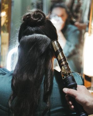 Professional hairstyling in progress with a curling iron being used on long dark hair.