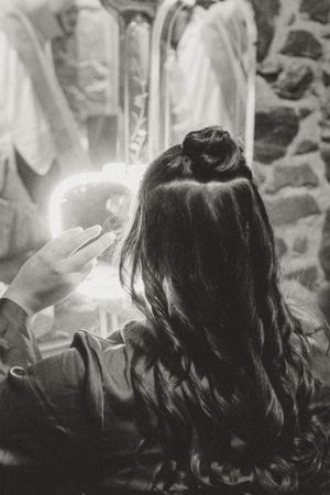Black and white photo of a woman with long dark hair getting ready in front of a mirror.