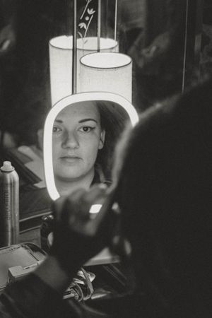 Artistic black and white mirror reflection showing a person with overhead lighting in a moody setting.