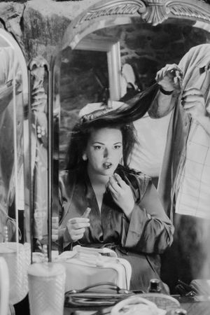 Vintage black and white photo of a woman applying makeup at a vanity table.