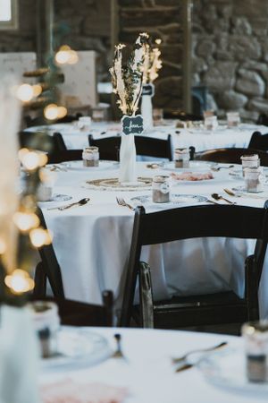 Elegant wedding reception table setting with white linens, black chairs and dried flower centerpiece.