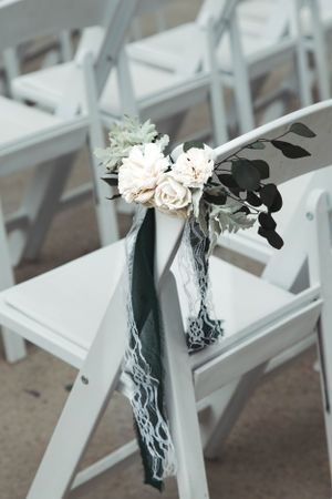 White folding chair decorated with delicate floral arrangement and gray fabric for wedding ceremony.