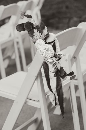 White folding chair decorated with floral arrangements and ribbons at a wedding ceremony.