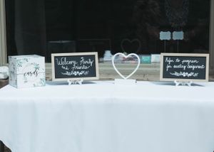 Wedding reception table with decorative signs and a white heart centerpiece on white tablecloth.