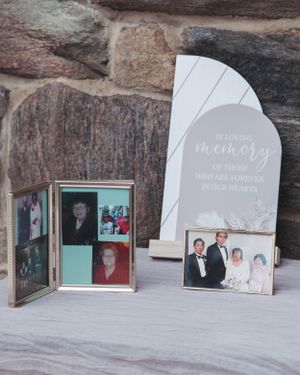 A memorial display with vintage photographs and a white decorative plaque against a stone wall background.