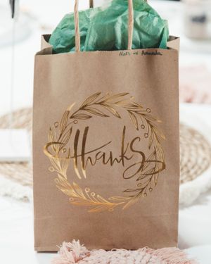 A brown paper gift bag with gold 'Thanks' text and floral wreath design.