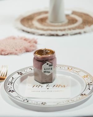 Elegant place setting with decorative plate and small pink favor jar.